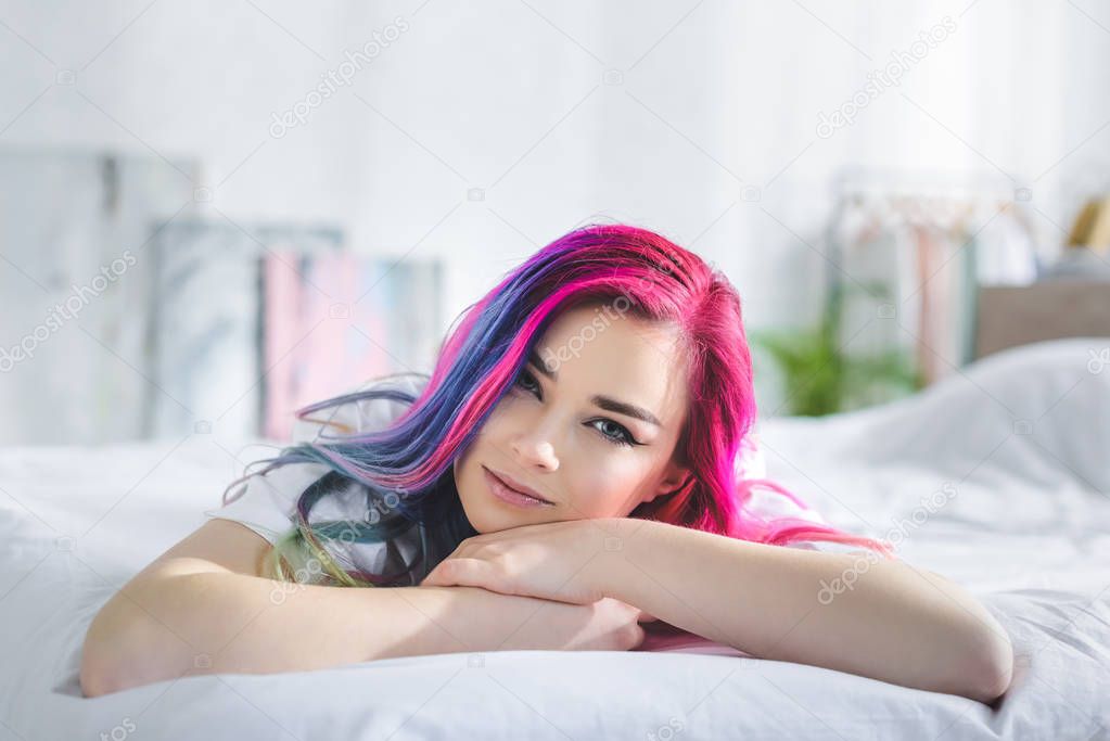 beautiful girl with colorful hair looking at camera and laying in bed