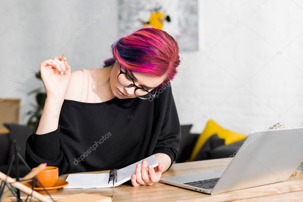 girl with colorful hair sitting at table and writing notes in notebook