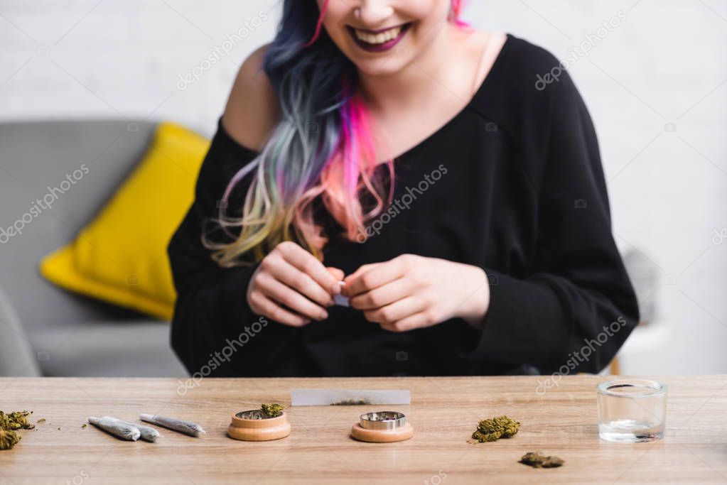 Cropped view of hipster girl smiling and making joint with medical cannabis
