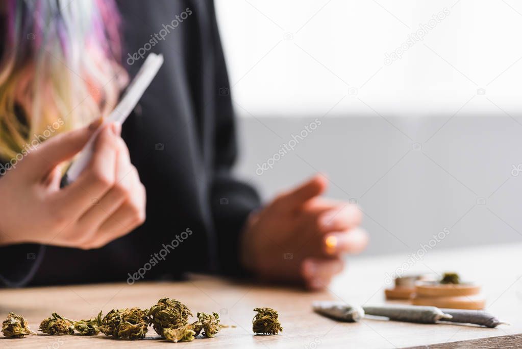 Cropped view of girl holding joint at table with medical marijuana