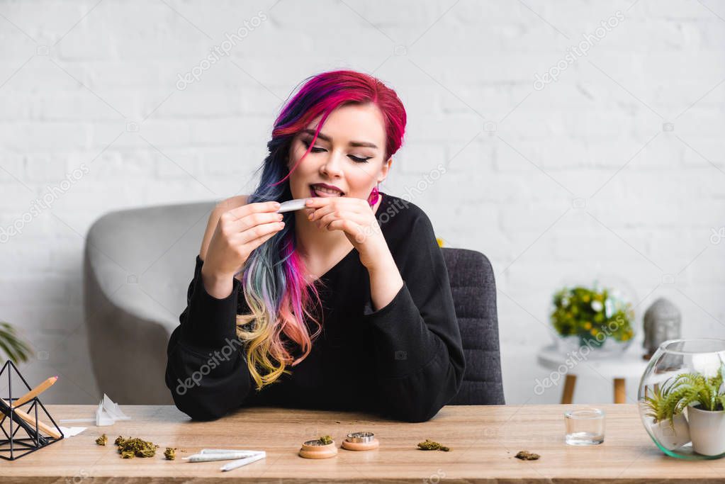  attractive girl licking joint with medical marijuana while sitting behind table in living room