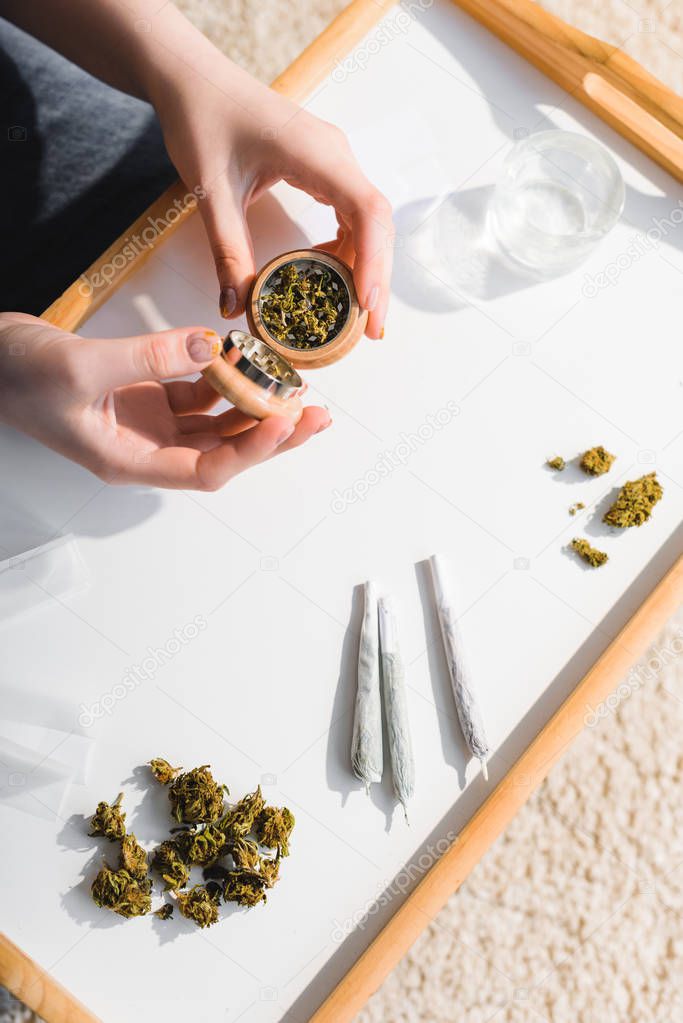 top view of girl closing herb grinder with medical cannabis in sunlight 