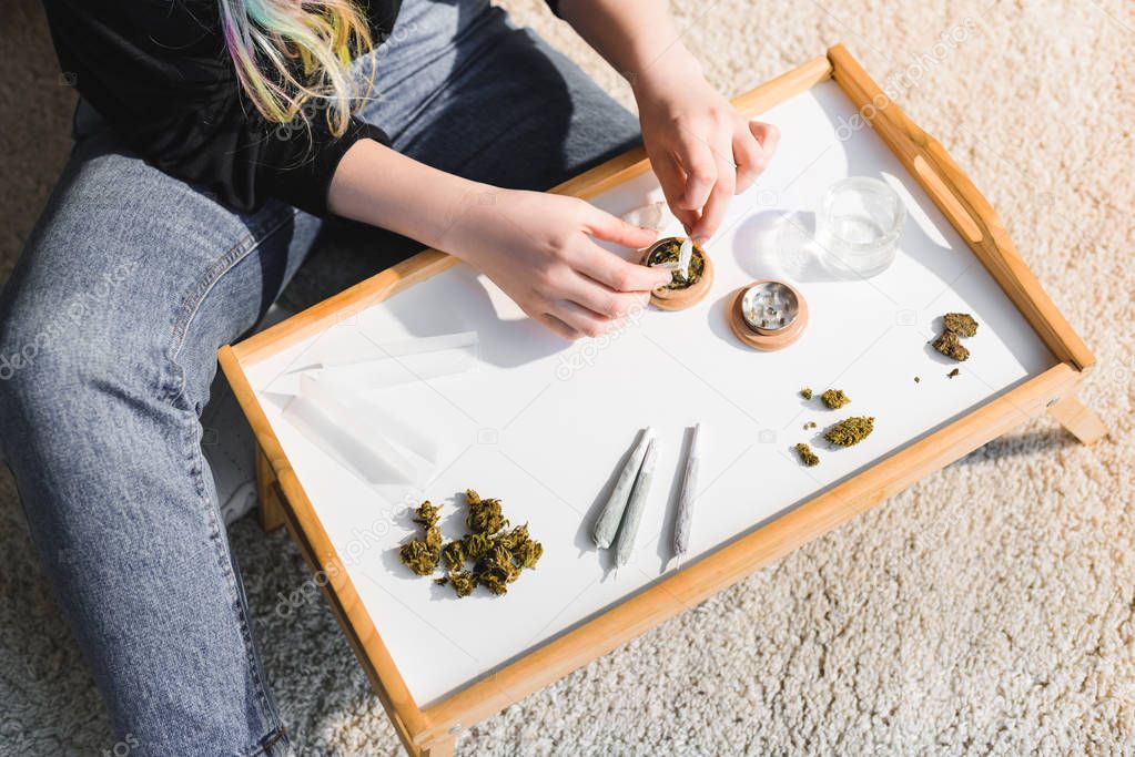 cropped view of girl putting medical cannabis in herb grinder