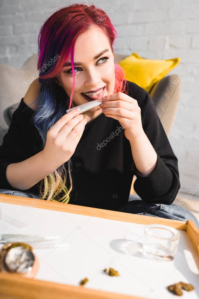 beautiful hipster girl licking joint, smiling and looking away