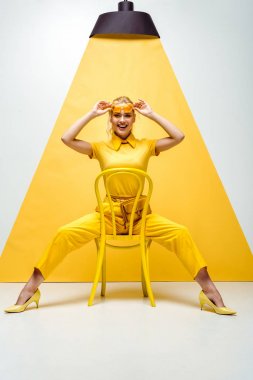 neşeli sarışın kadın güneş gözlüğü dokunmadan ve beyaz ve sarı sandalyede oturan 