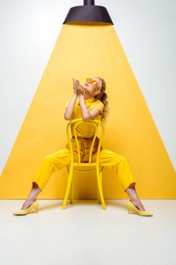 güneş gözlüğü sarışın kadın sandalyede oturan ve sarı ve beyaz lamba bakarken hava öpücük gönderme