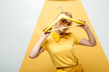 beyaz ve sarı üzerinde askı tutarken yüzünü kaplayan güneş gözlüğü çekici sarışın kadın 