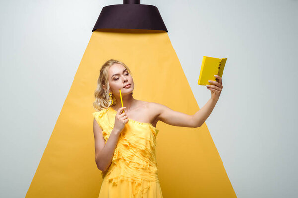 pensive woman looking at notebook while posing on white and yellow 