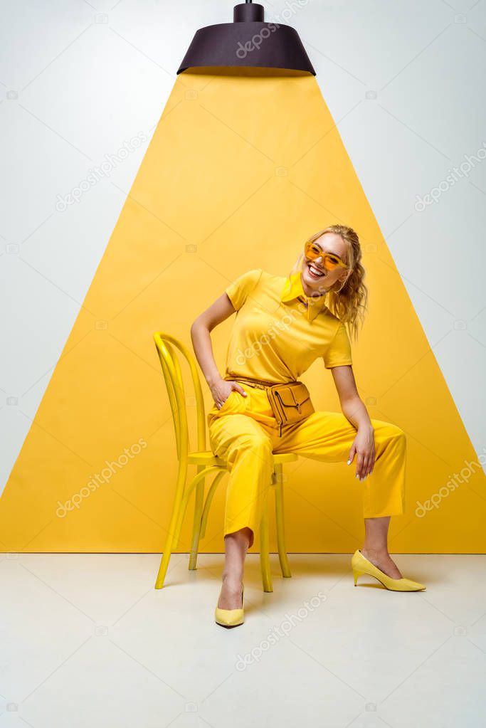 cheerful blonde woman in sunglasses sitting on chair on white and yellow 