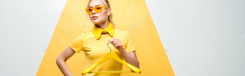 panoramic shot of attractive woman in sunglasses holding hanger on white and yellow 