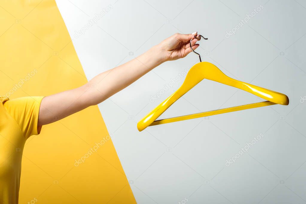 cropped view of woman holding wooden hanger on white and yellow 