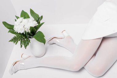 beyaz çiçek buketi ile vazo yakınında oturan kadın kırpılmış görünümü 