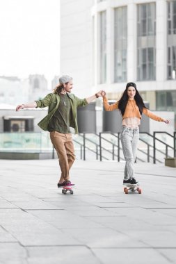 neşeli kadın erkekle el ele tutuşuyor, şehirde kaykaylara biniyor