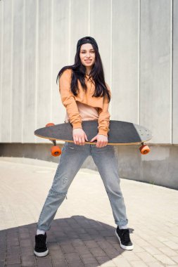young woman standing near concentrate wall, holding skateboard in hand