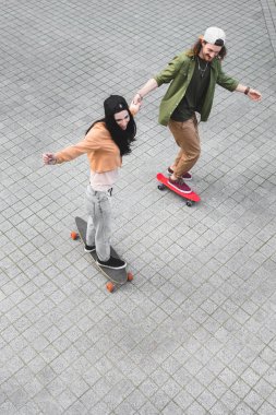 high angle view of happy couple holding hands, smiling and riding on skateboards clipart