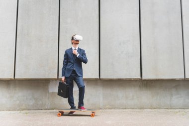 resmi giyim ve vr kulaklık beton duvar arka plan üzerinde longboard yakınında duran işadamı