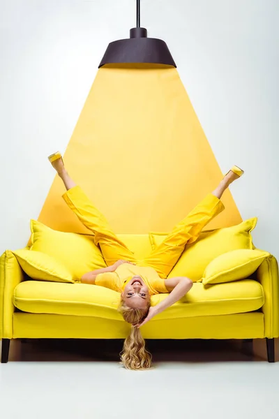 stock image happy blonde woman lying upside down on sofa on white and yellow 