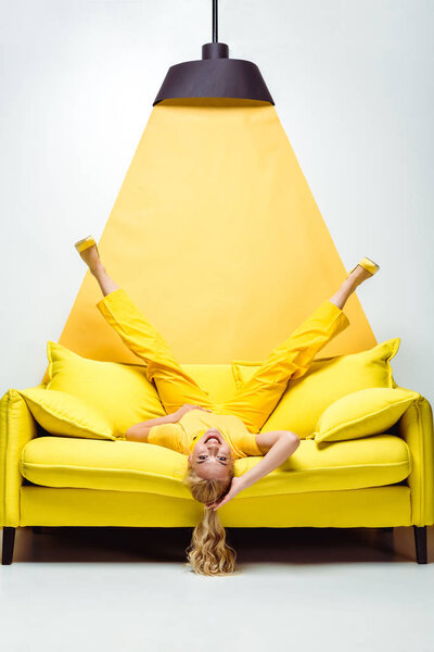 happy blonde woman lying upside down on sofa on white and yellow 