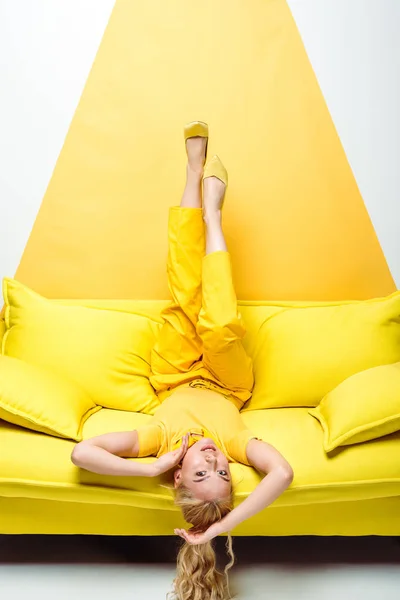 attractive blonde woman lying upside down on sofa on white and yellow