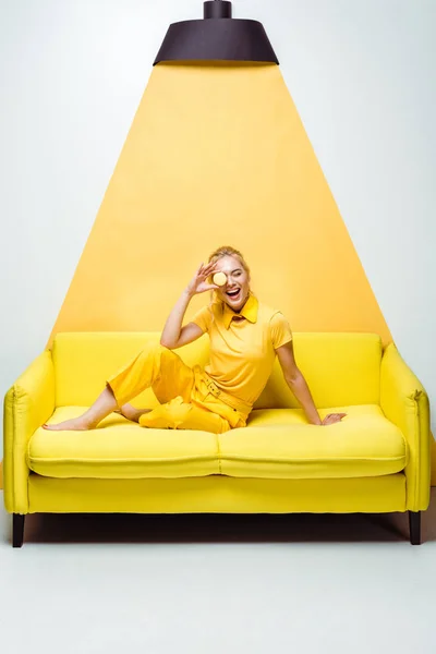 Веселая Блондинка Сидящая Диване Покрывающая Лицо Вкусным Макароном Белом Желтом — стоковое фото