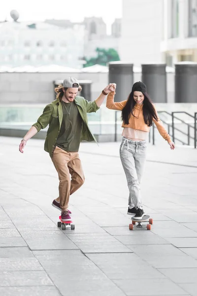 Šťastný Muž Držící Ruce Krásnou Ženou Jezdila Skateboard Městě — Stock fotografie