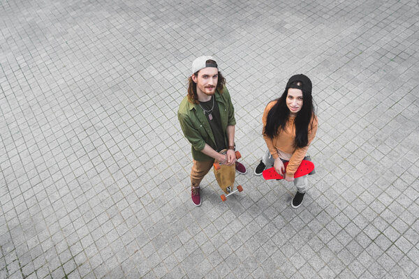 high angle view of beautiful woman and man standing with skateboards, looking at camera