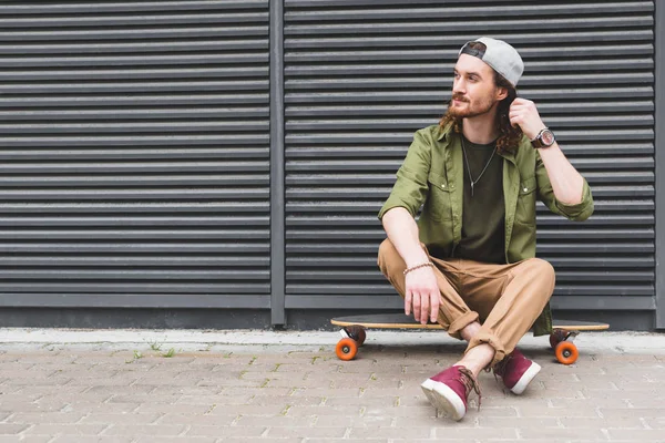 calm and handsome man sitting on skateboard, looking away