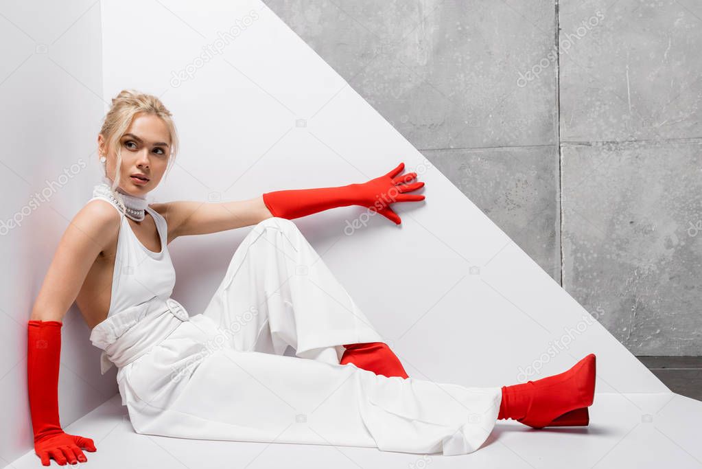 attractive and stylish woman sitting in red gloves and shoes on white and grey 