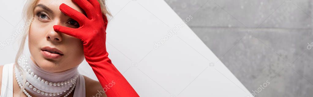 panoramic shot of stylish woman in red glove covering face on white and grey 
