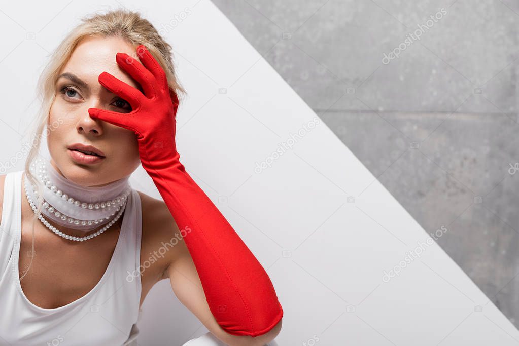 stylish woman in red glove covering face on white and grey 