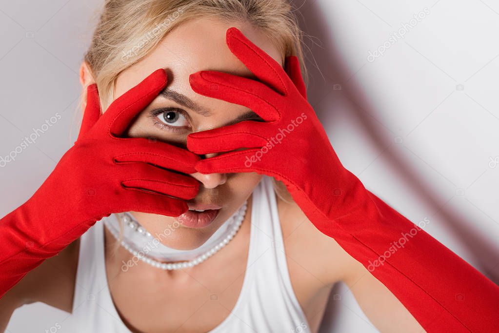 blonde young woman in red gloves covering face on white 