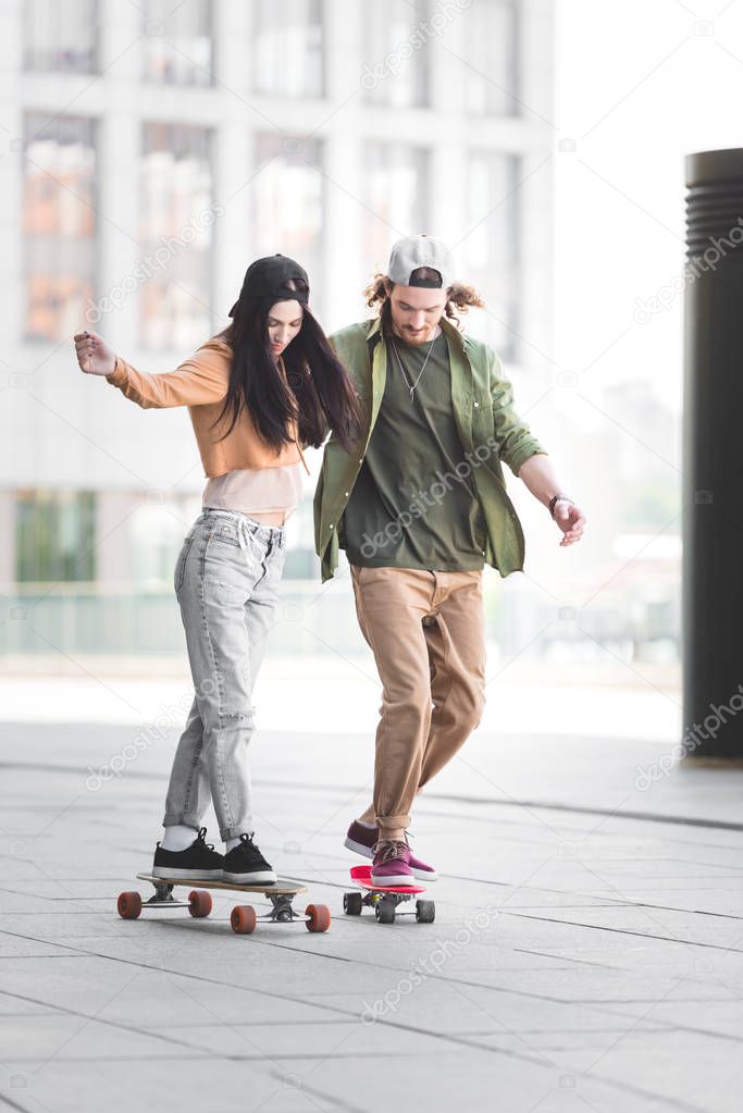 happy couple in casual wear riding on skateboards in city