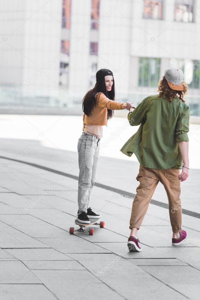 beautiful woman holding hands with man, riding on skateboard in city