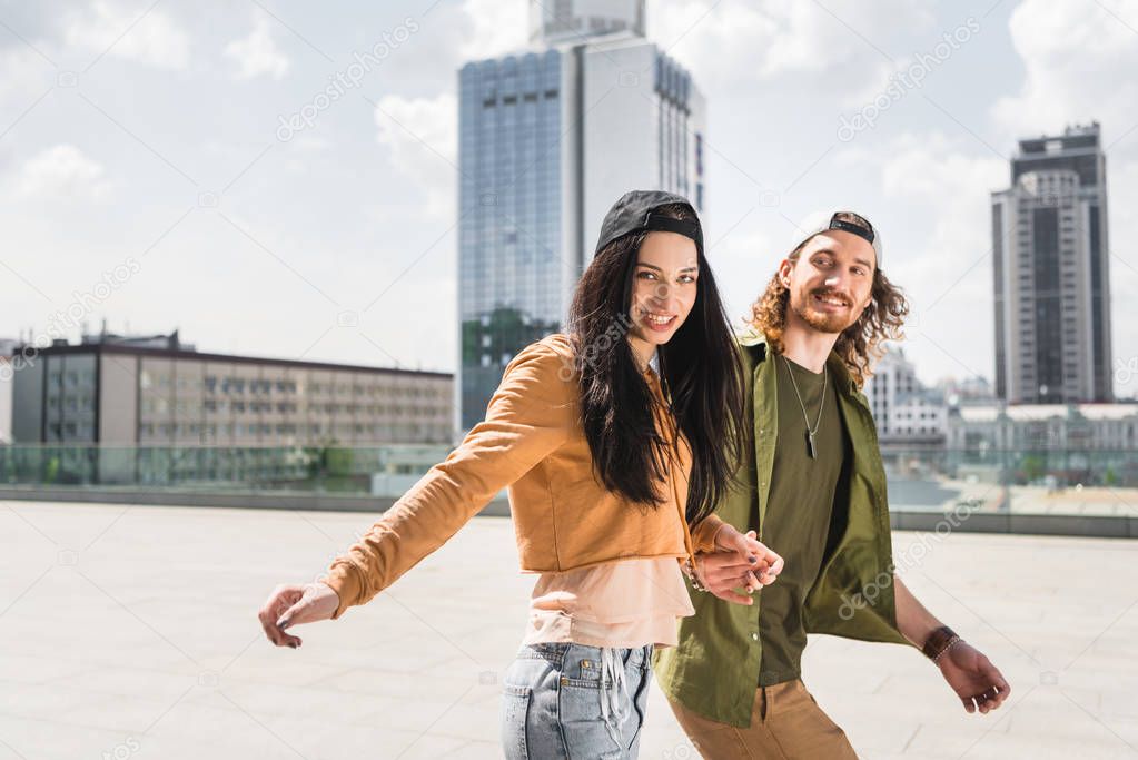 happy couple in casual wear holding hands, walking on street, looking at camera