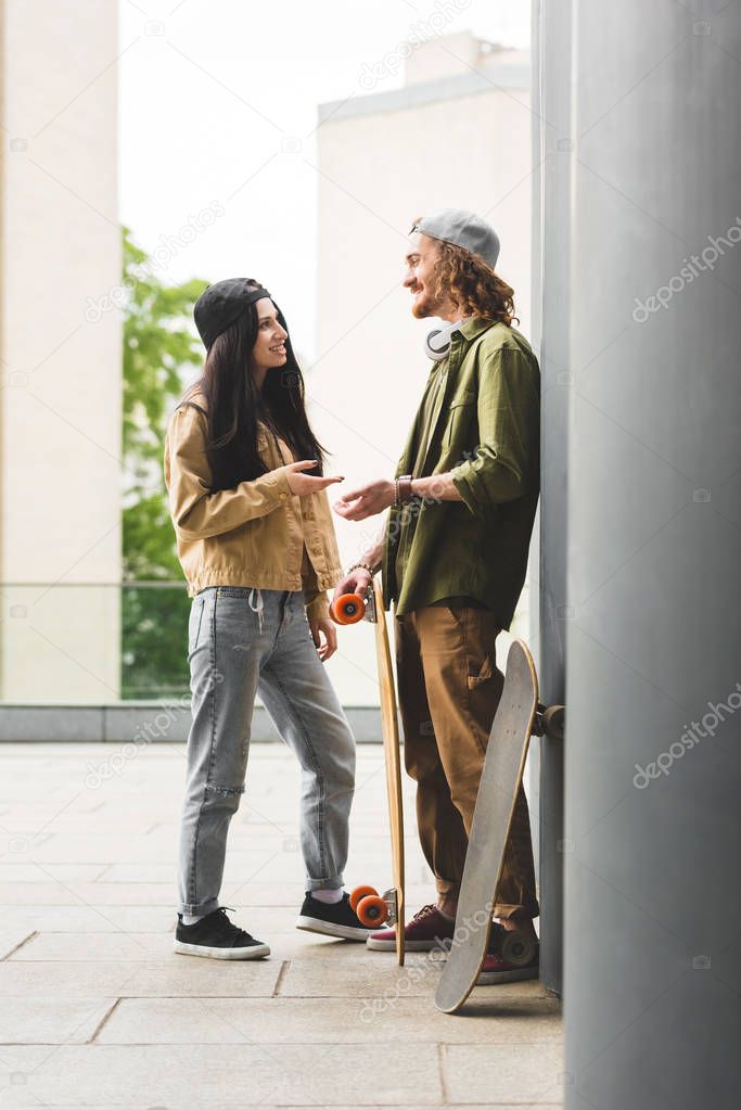 side view of handsome man and woman with skateboards standing on rooftop, looking at each other