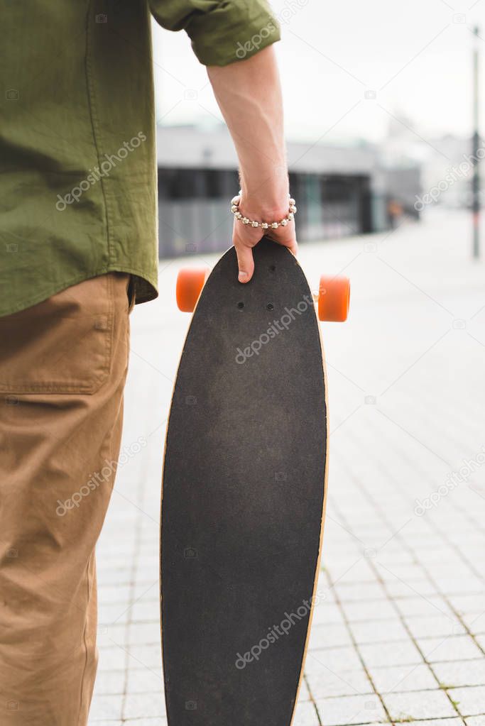 cropped view of man in casual wear standing with skateboard in hand