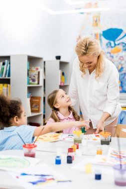 mutlu çok kültürlü çocukların yanında dururken neşeli öğretmenin gülümseyen seçici odak 