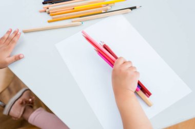 cropped view of kid holding colorful pencils near paper  clipart