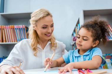 selective focus of cheerful woman looking at cute african american kid  clipart