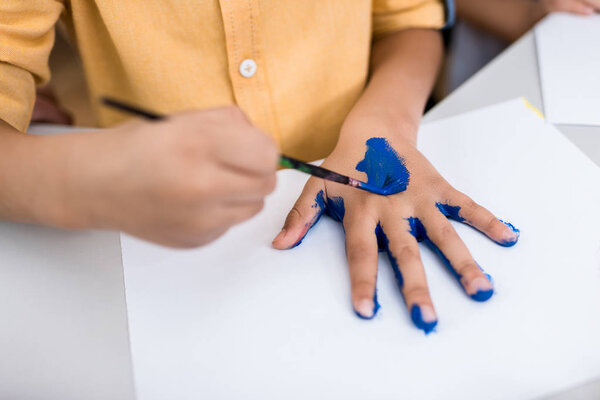 обрезанный вид ребенка, держащего кисть при рисовании на руке
 