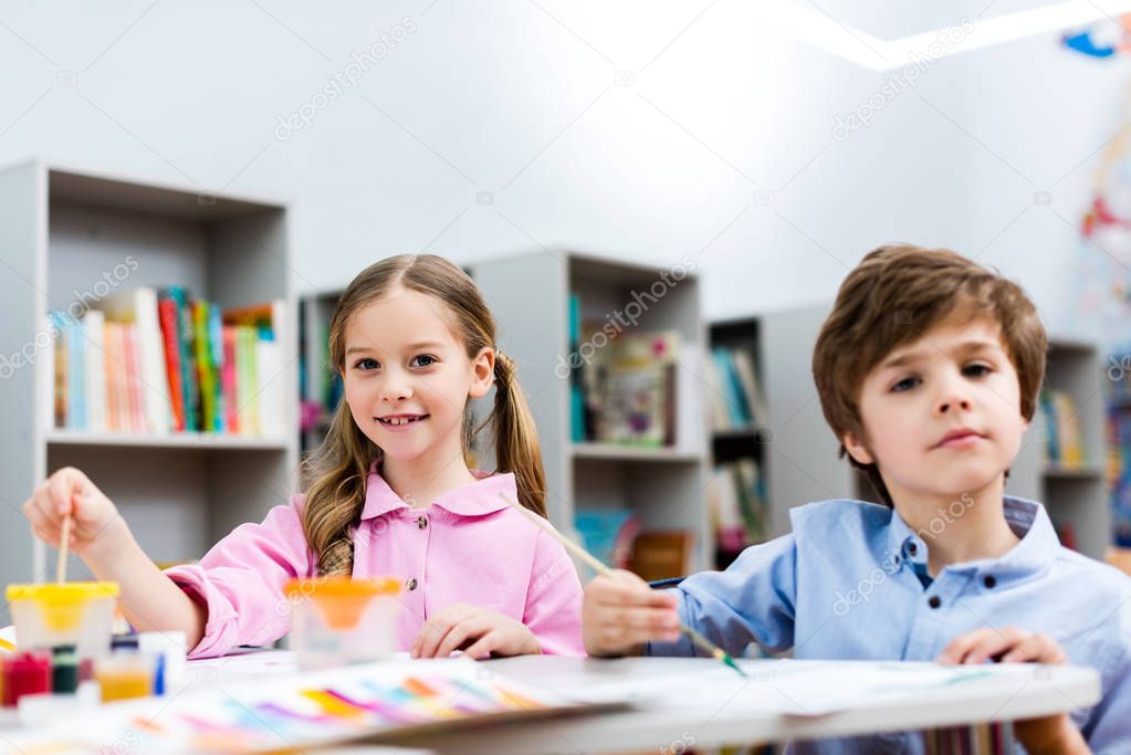 selective focus of smiling child near cute boy holding paintbrush 