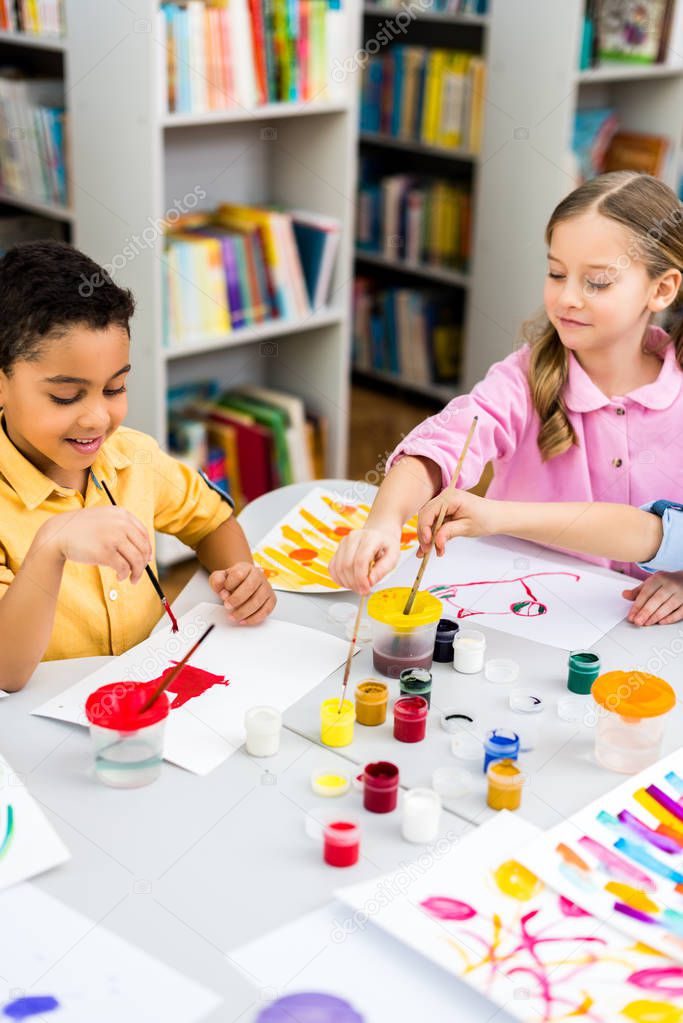 selective focus of happy multicultural kids painting on papers 