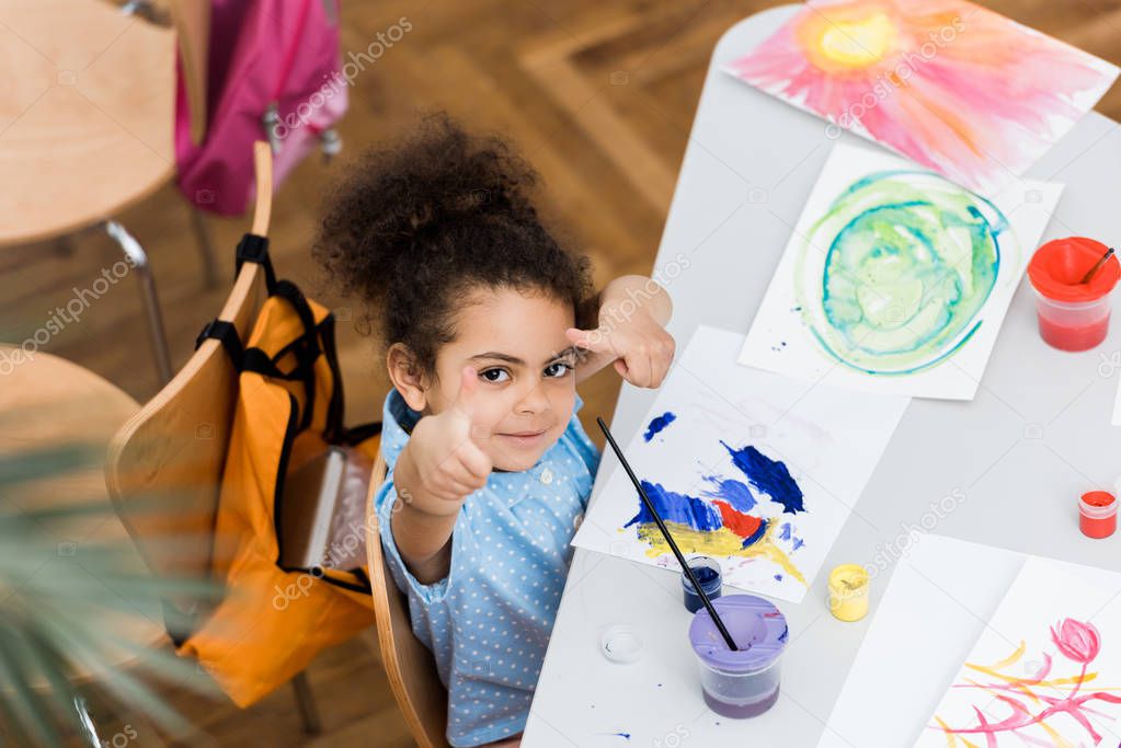 overhead view of cute african american kid pointing with fingers near paper with painting 