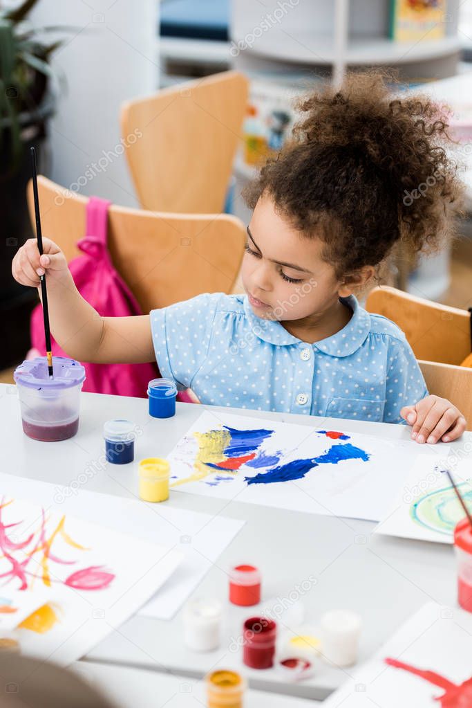 selective focus of african american child holding paintbrush near paper with drawing 