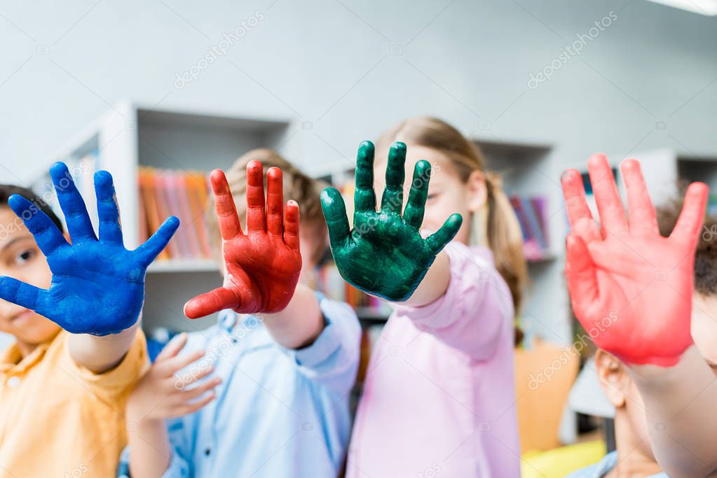 selective focus of multicultural kids covering faces with colorful hands 