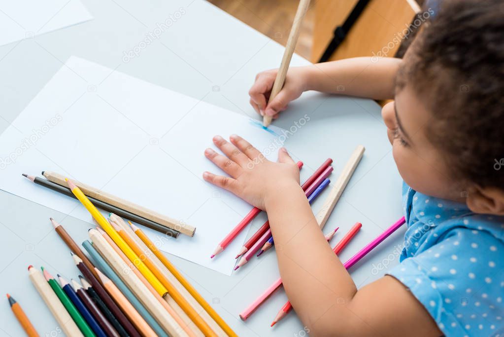 overhead view of cute african american kid drawing on blank paper 