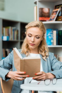kütüphanede oturan ve kitap okuma çekici ve odaklı sarışın kadın 