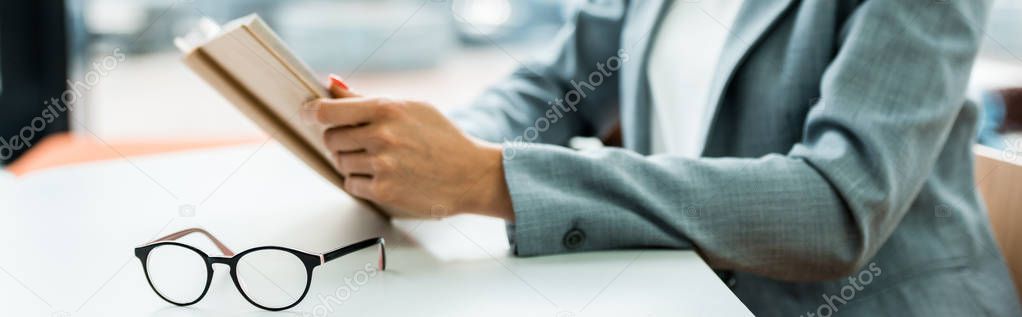 panoramic shot of glasses on table near woman holding book 