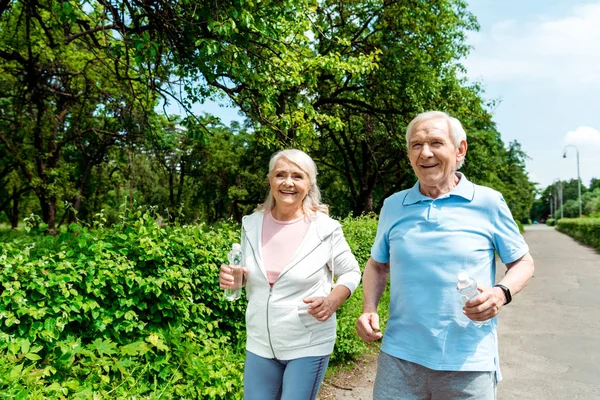 Happy Senior Woman Holding Bottle Water While Running Husband Park — Stock Photo, Image