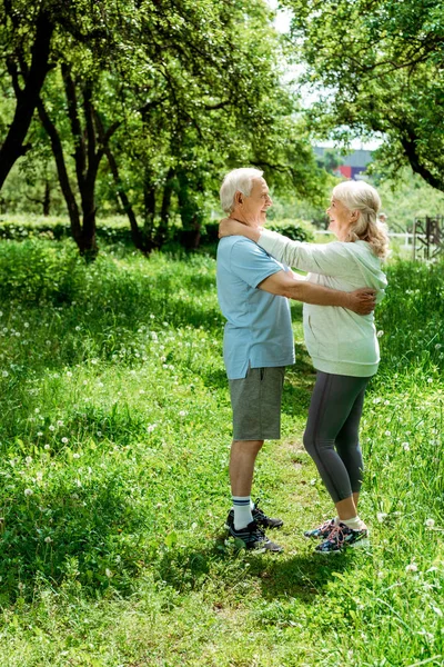 緑の公園に立っている間 幸せな先輩妻を抱きしめる笑顔の引退した男 — ストック写真